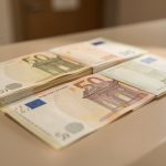 Billets en euros disposés sur un comptoir bancaire, éclairés latéralement pour faire ressortir les reliefs et les éléments de sécurité.