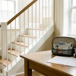 Intérieur lumineux avec un escalier équipé d’une rampe sécurisée, une trousse de premiers secours et des papiers vierges posés sur une table en bois.